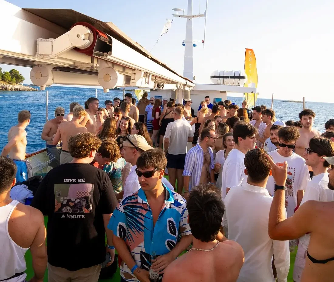 Luxurious party yacht sailing at sunset in Pula during Boom Boat Party 2026 with people dancing on deck.
