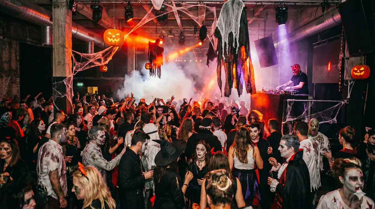 Crowd in scary costumes dancing at Club Uljanik during Halloween Madness party in Pula with spooky decorations and red lighting.